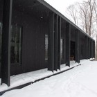 Черный дом контрастирует с заснеженным зимним лесом.