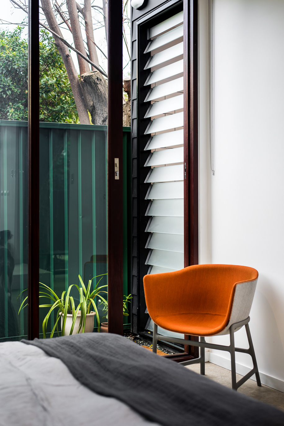 Удобное оранжевое кресло в спальне рядом со сдвижной стеклянной дверью в сад.