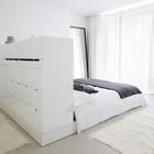 Современная белая кровать с большой системой хранения в изголовье, которая является частью гардероба.