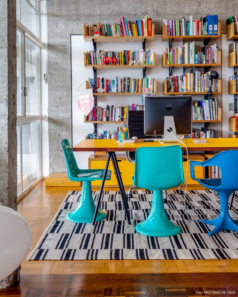 Домашний офис в ярких тонах с большим столом в центре и открытыми стеллажами для книг.
