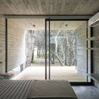 Спальня также выдержана в минималистическом стиле с бетонными полками. Стена выходящая на террасу с деревянным настилом полностью стеклянная со сдвижной дверью.