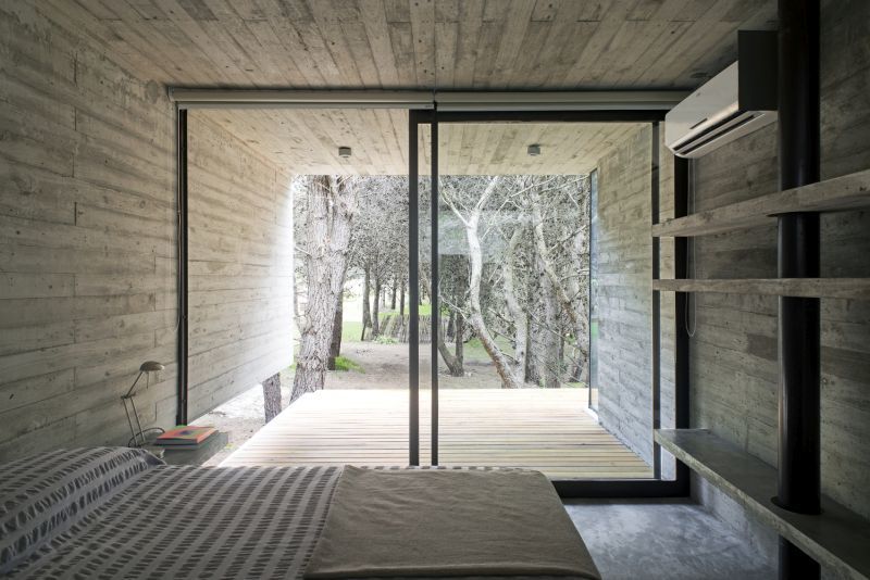 Спальня также выдержана в минималистическом стиле с бетонными полками. Стена выходящая на террасу с деревянным настилом полностью стеклянная со сдвижной дверью.