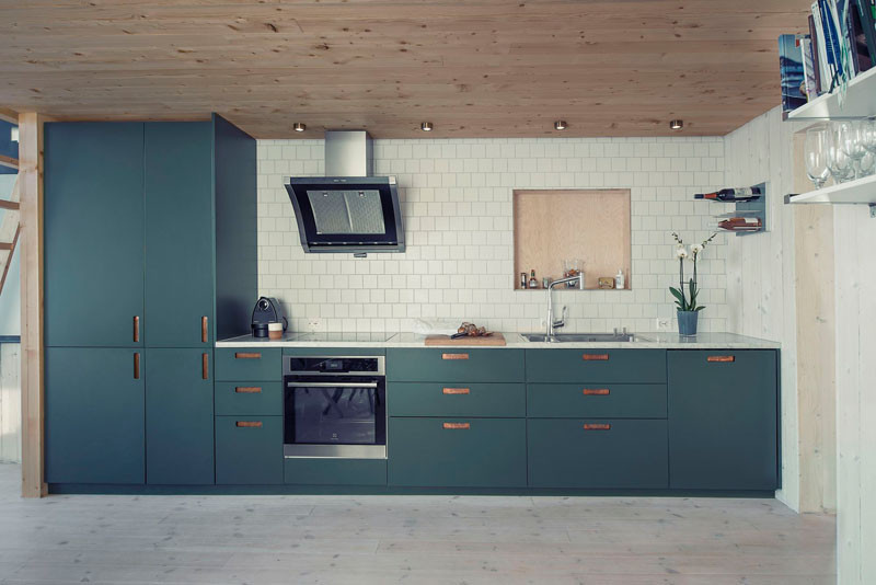 Кухня расположена вдоль одной из стен жилой комнаты и не концентрирует на себе внимания. А кухонные фасады темно-бирюзового цвета разнообразят и украшают пространство.