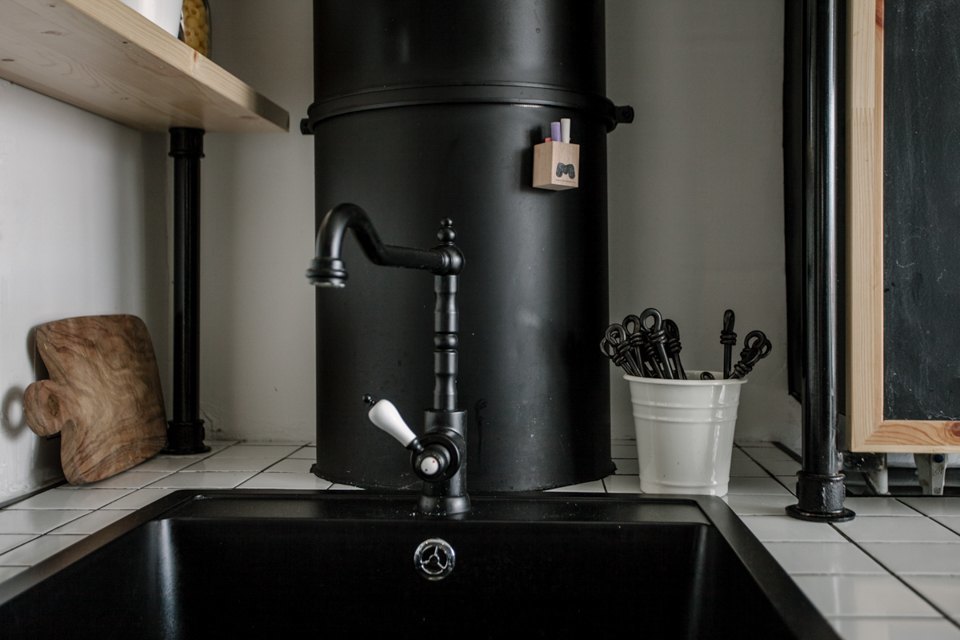 Винтажного вида черный кран на кухне не выделяется на фоне черной вентиляционной трубы, а выглядит стильно и органично