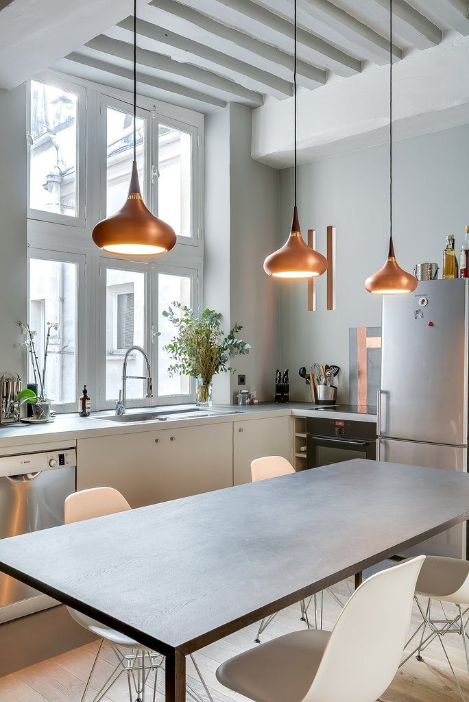 Яркие светильники над обеденным столом оживляют серый интерьер кухни-столовой