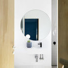 Белая и светлая ванна с простым белым кафелем на полу и в душе. Круглое зеркало повторяет формой окна дома.