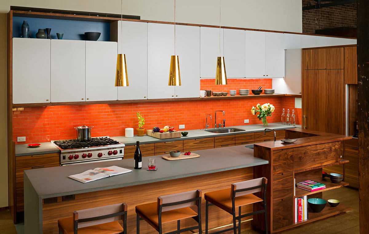 Яркий оранжевый кафель кухонного фартука делает интерьер ярче и жизнерадостней. Кухонный остров традиционно служит барной стойкой.