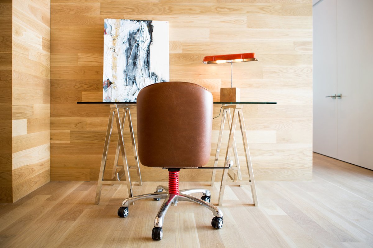 Минималистский домашний офис со стенами и полом отделанными стенами, кожаным креслом и стеклянным рабочим столом.
