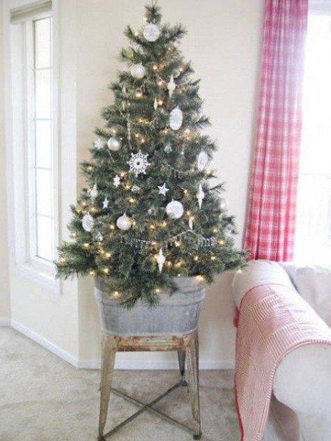 Маленькое дерево в цинковом ведре украшенное белыми украшениями, снежинками и гирляндами.