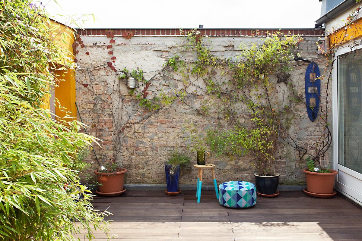 Озелененная терраса с заплетенной плющем кирпичной стеной напоминает небольшой дворик.
