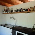 Дровяная печь, кухонная раковина и открытая полка на стене для хранения кухонных принадлежностей.