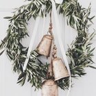 Рустикальный венок из оливковых ветвей с колокольчиками и бантом из белой ленты.