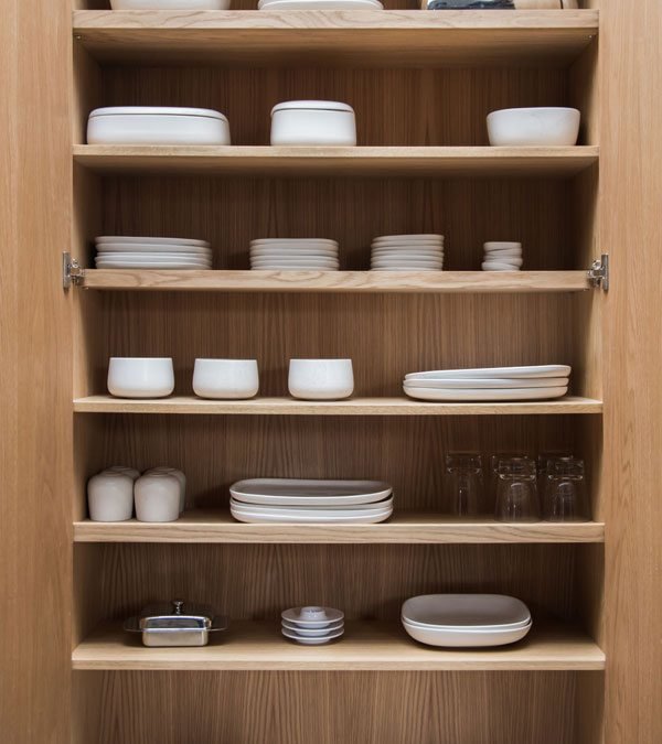 Не глубокий шкаф с полками для хранения посуды спрятан в стене рядом с кухней.