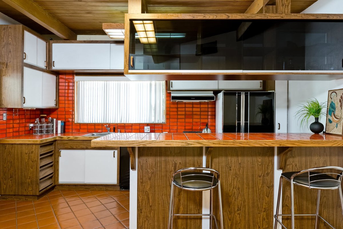 Красная кафельная плитка оживляет кухню. Над барной стойкой в воздухе висит остекленная с двух сторон темным стеклом полка для посуды.