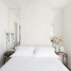 В спальне изголовье кровати из крашеного в белый кирпича обрамлено узкими вертикальными зеркалами, которые придают глубины небольшому помещению.