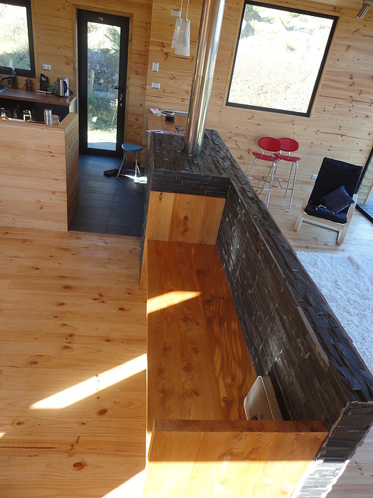 Разделительная перегородка между гостиной и столовой с кухней. С одной стороны от камина находится барная стойка, а с другой (в гостиной) удобная деревянная скамейка.
