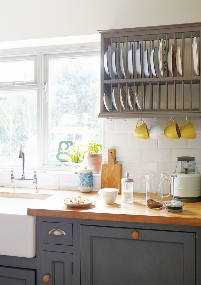 Лакированная деревянная кухонная столешница контрастирует с темным цветом кухонных шкафчиков и сушилкой для тарелок